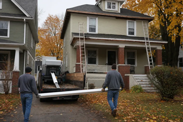 Seamless gutter machine on a work truck extruding a long aluminum run while two technicians carry it toward a Lakewood house